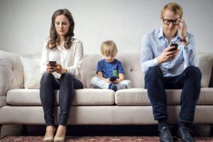 Young family is sitting on the couch and using mobile phones