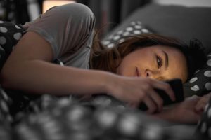 Girl using smart phone and lying down in bed late at night texting her therapist