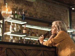 Pretty blonde woman sitting at the bar counter and seeping beer while being upset with something