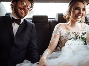 Newlyweds holding hands in the backseat