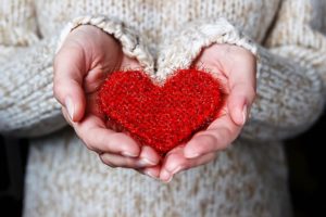 Girl in a light sweater gives a knitted heart. Close-up